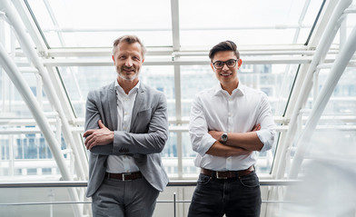 Businessman and trainee stand in the office with their arms crossed